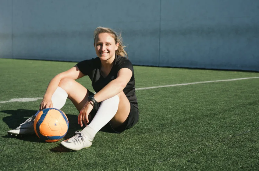 Jogadora de futebol sentada no gramado contente com sua chuteira no tamanho certo.